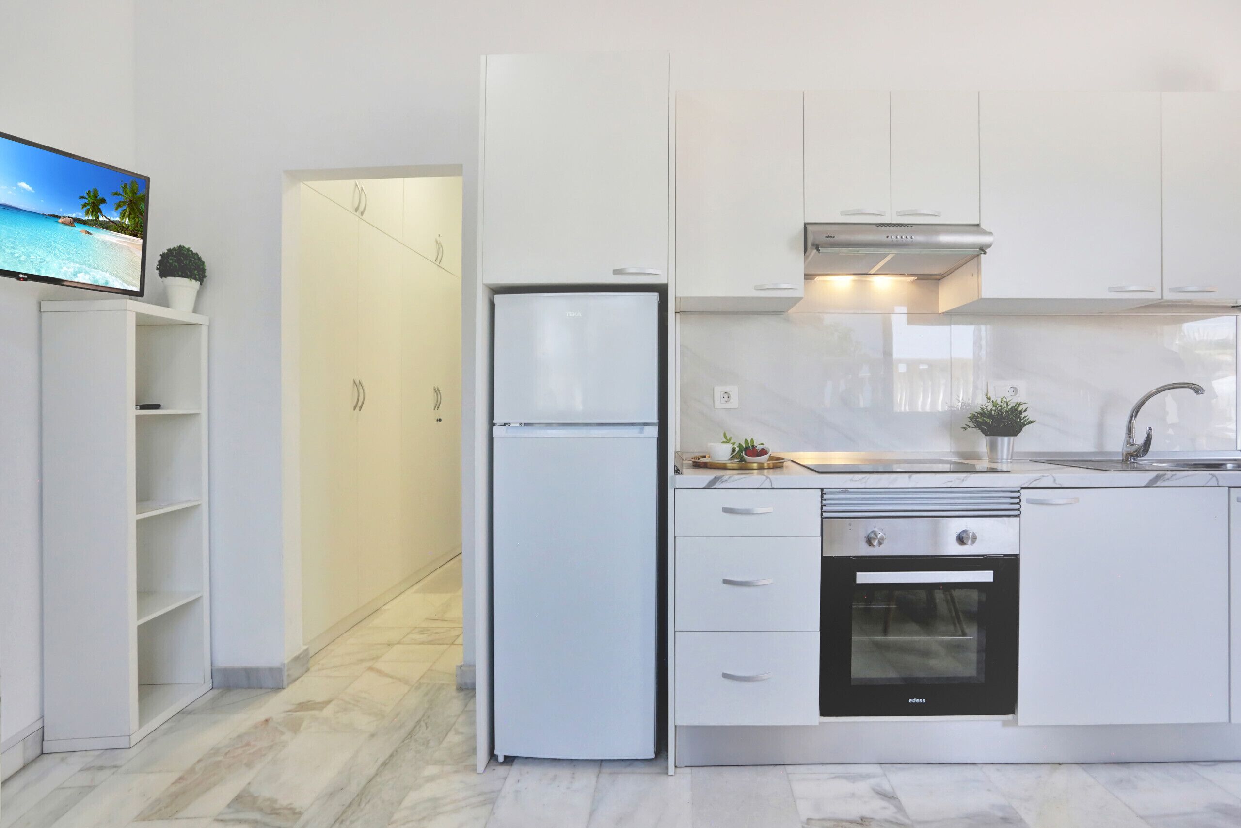 Una cocina moderna con armarios blancos, horno integrado y refrigerador.