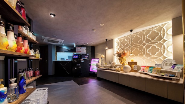 A hotel reception area with a counter displaying various products, a digital screen, and a decorative wall. - MANORHOUSE - Adult Only (Warabi)