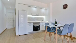 A modern kitchen with white cabinets, a built-in oven, and a dining area with a glass table and blue chairs.