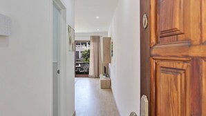 A hallway with a wooden door, a white wall, and a view into a balcony area with a table and chairs.