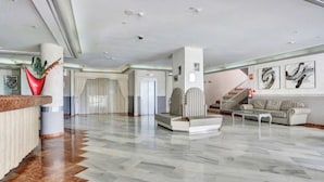 Un vestíbulo amplio con piso de mármol, un mostrador de recepción, un sofá a rayas y una escalera.