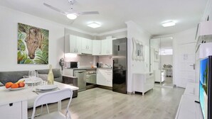 Una cocina moderna con armarios blancos, un comedor con una mesa preparada para dos personas y un cuadro grande en la pared.