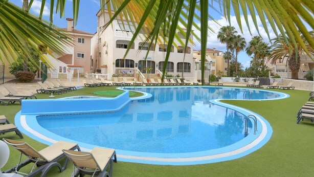 Una piscina con múltiples carriles, rodeada de sillas de descanso y palmeras.