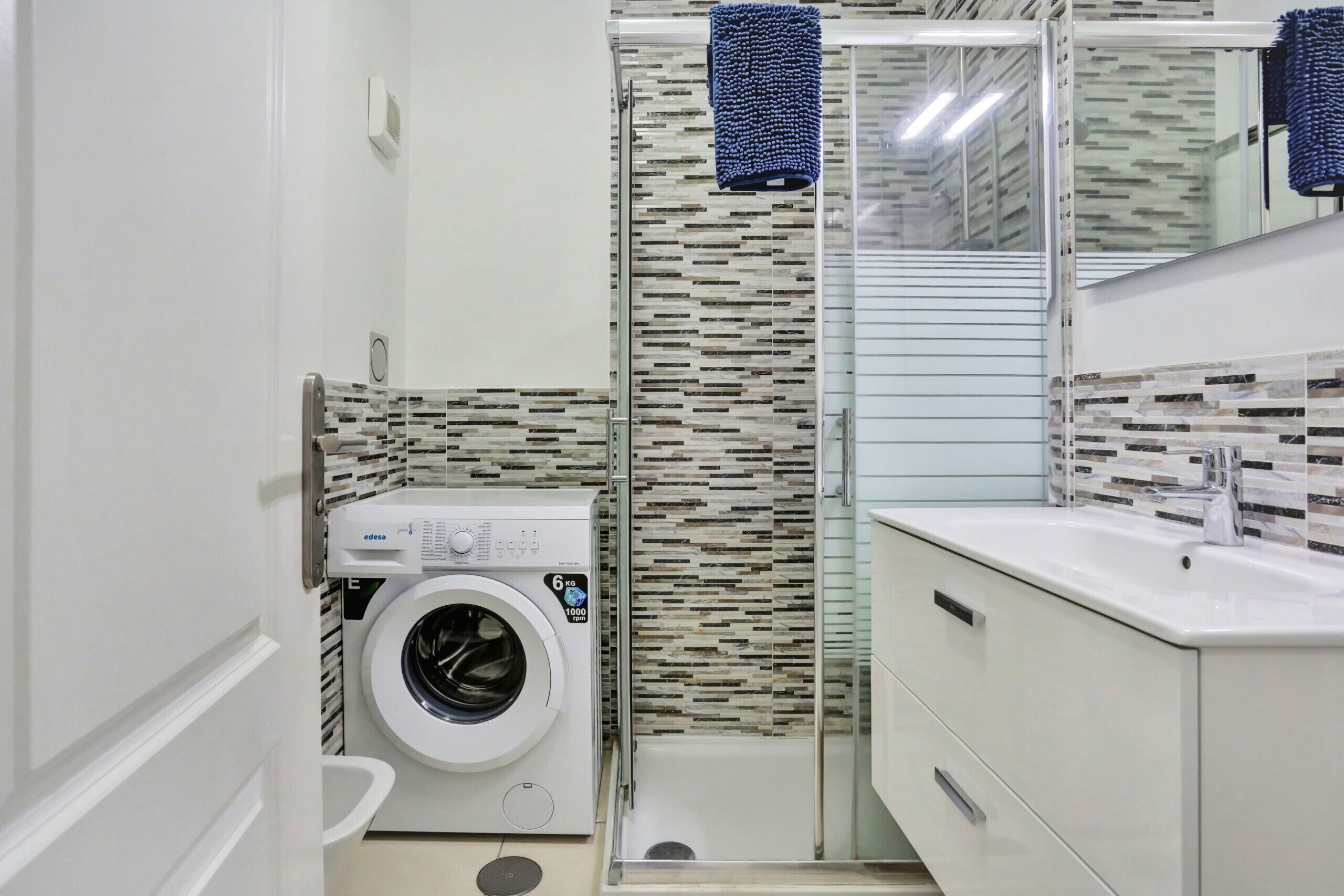 A compact bathroom with a washing machine, a glass shower enclosure, and a modern vanity.