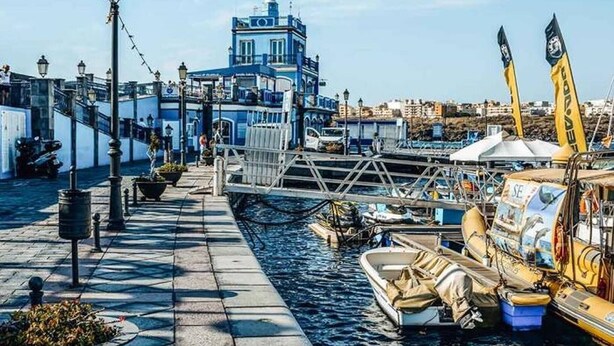 Un paseo marítimo con un puente, barcos y un edificio de fachada azul.