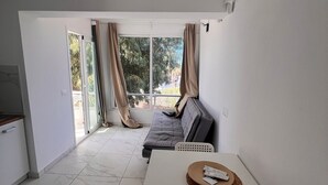 Una habitación moderna con una mesa blanca, un sofá gris y vistas al exterior a través de una puerta corredera de vidrio.