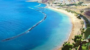 Vista aérea de una zona costera con una playa, aguas azules cristalinas y un pueblo con edificios en una ladera.