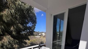 Un balcón con una mesa y sillas, vista del paisaje y una puerta corredera de vidrio.