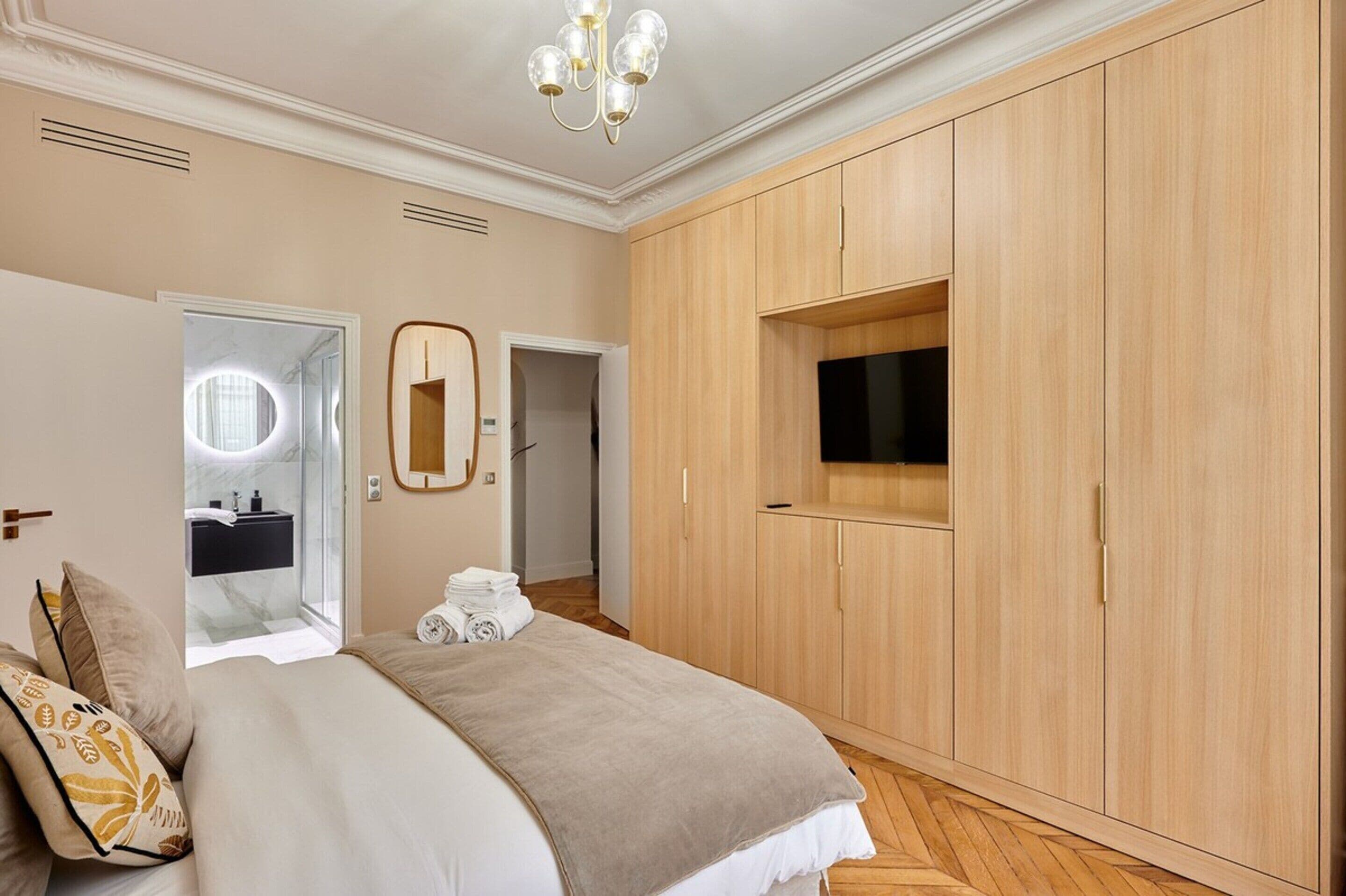 A bedroom with a large bed, a wardrobe, a mirror, and a TV.