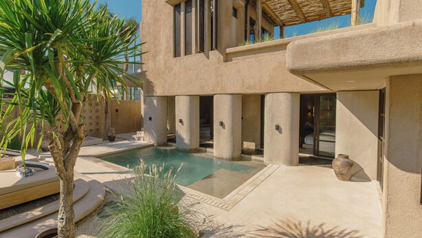 Un bâtiment moderne doté d’une piscine, de colonnes et d’un palmier.