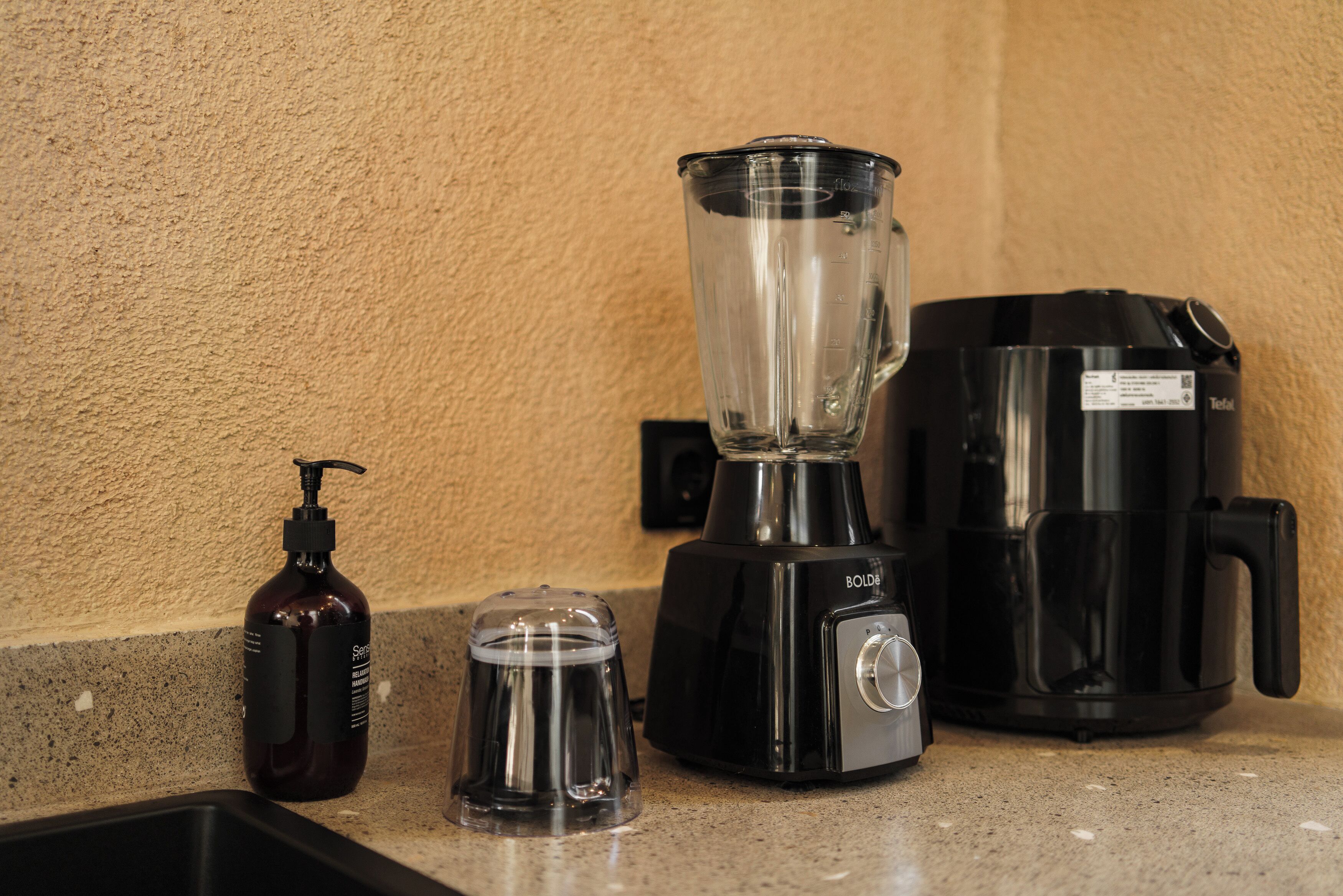 Un plan de travail de cuisine avec un mixeur, une machine à café et une bouteille de gel hydroalcoolique.