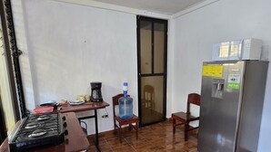 A compact kitchen with a gas stove, a refrigerator, a water dispenser, and a coffee maker. - Apartamentos el viajero (Panajachel)