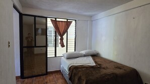 A bedroom with a bed, a window with curtains, a sliding door, and a ceiling light. - Apartamentos el viajero (Panajachel)