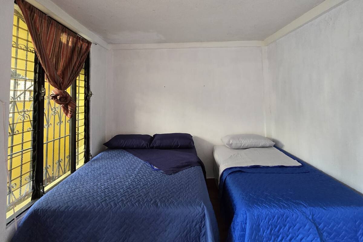 A small room with two single beds, a window with curtains, and a light fixture on the ceiling.