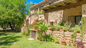A stone building with a covered porch, surrounded by a well-maintained garden with various potted plants and flowers. - Can Ferrer - Villa With Private Pool In Pollença (PollenÇa, Illes Balears)