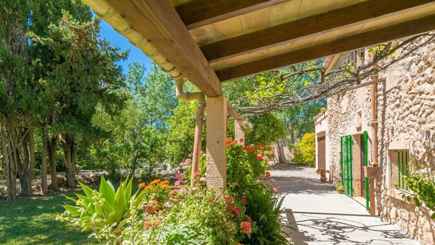 A stone building with a green door, surrounded by lush greenery and flowering plants. - Can Ferrer - Villa With Private Pool In Pollença (PollenÇa, Illes Balears)