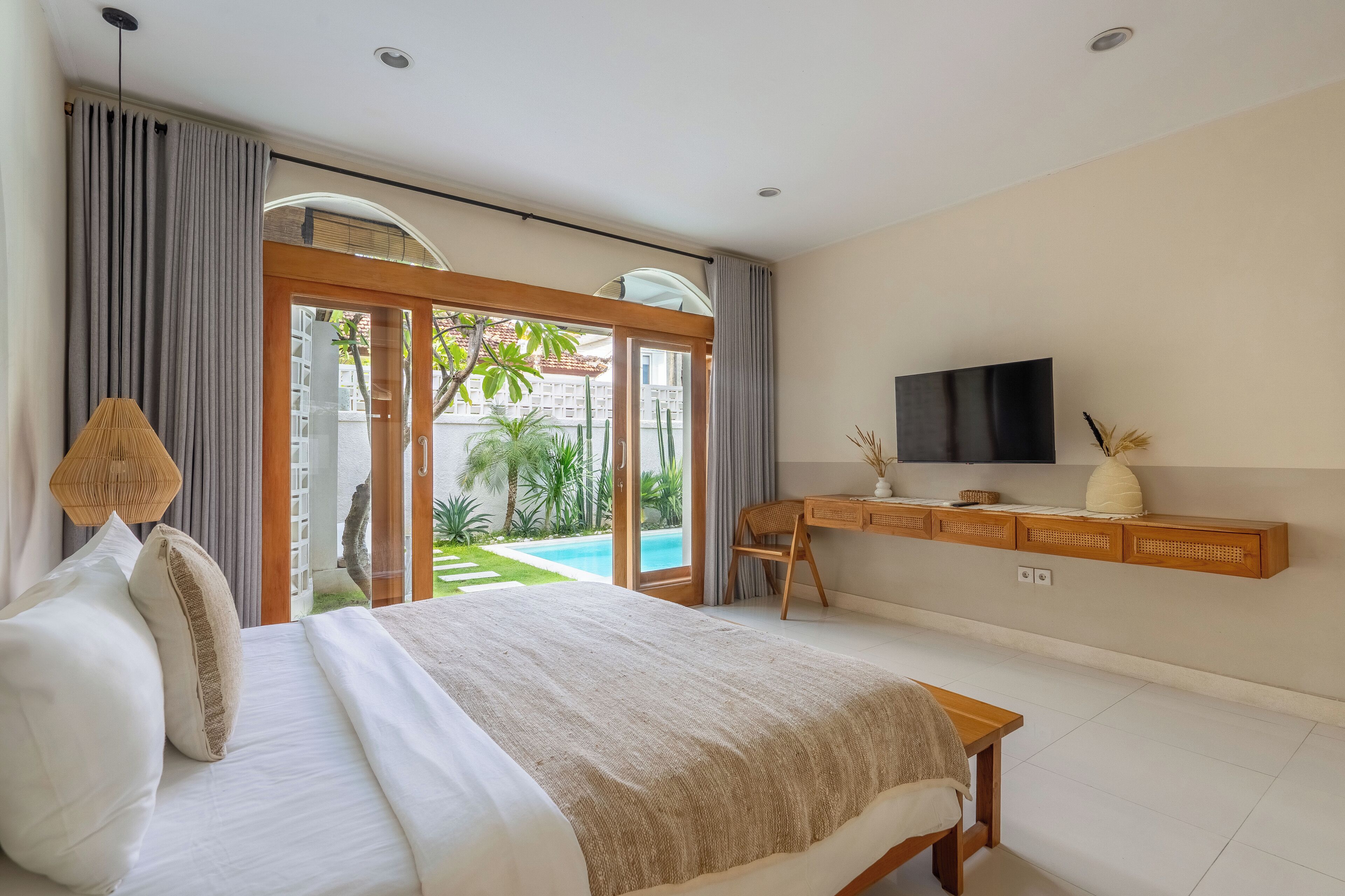 Ein Schlafzimmer mit Bett, Schreibtisch, Fernseher und Blick auf Pool und Grünflächen.