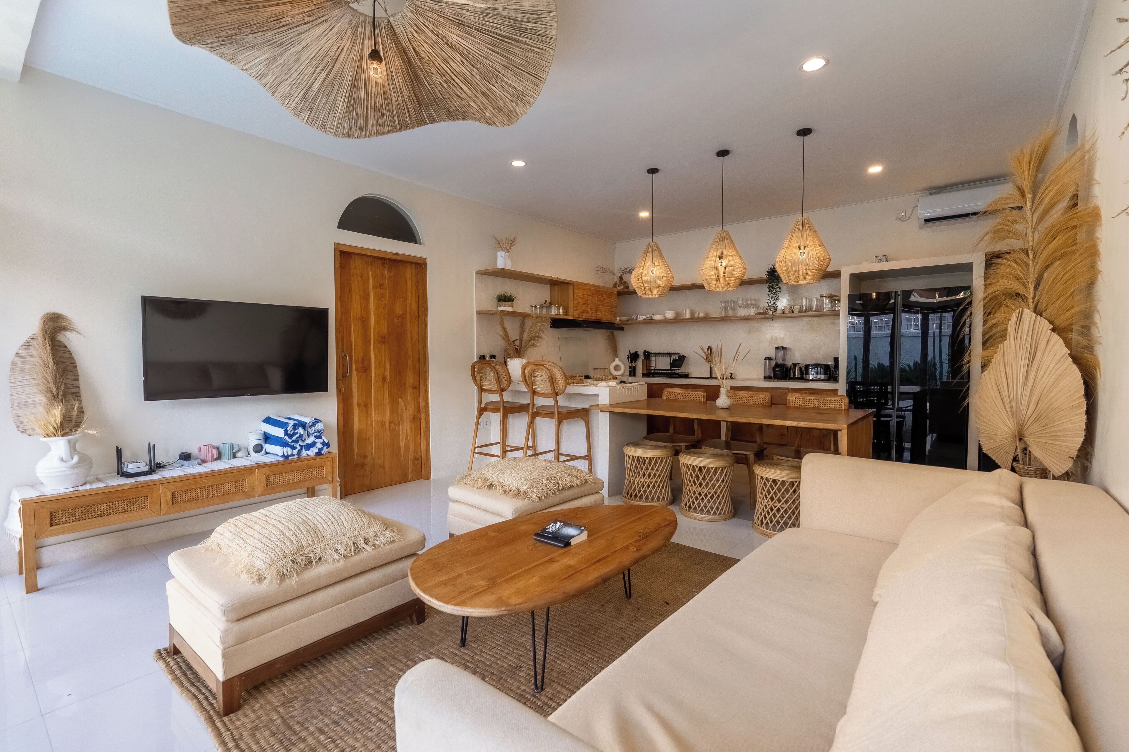 A modern living room with a sofa, coffee table, and TV. There is a kitchen area with a dining table and chairs.