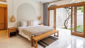 Ein modernes Schlafzimmer mit einem großen Bett, einer hölzernen Bank und Blick auf einen Garten durch Glastüren.