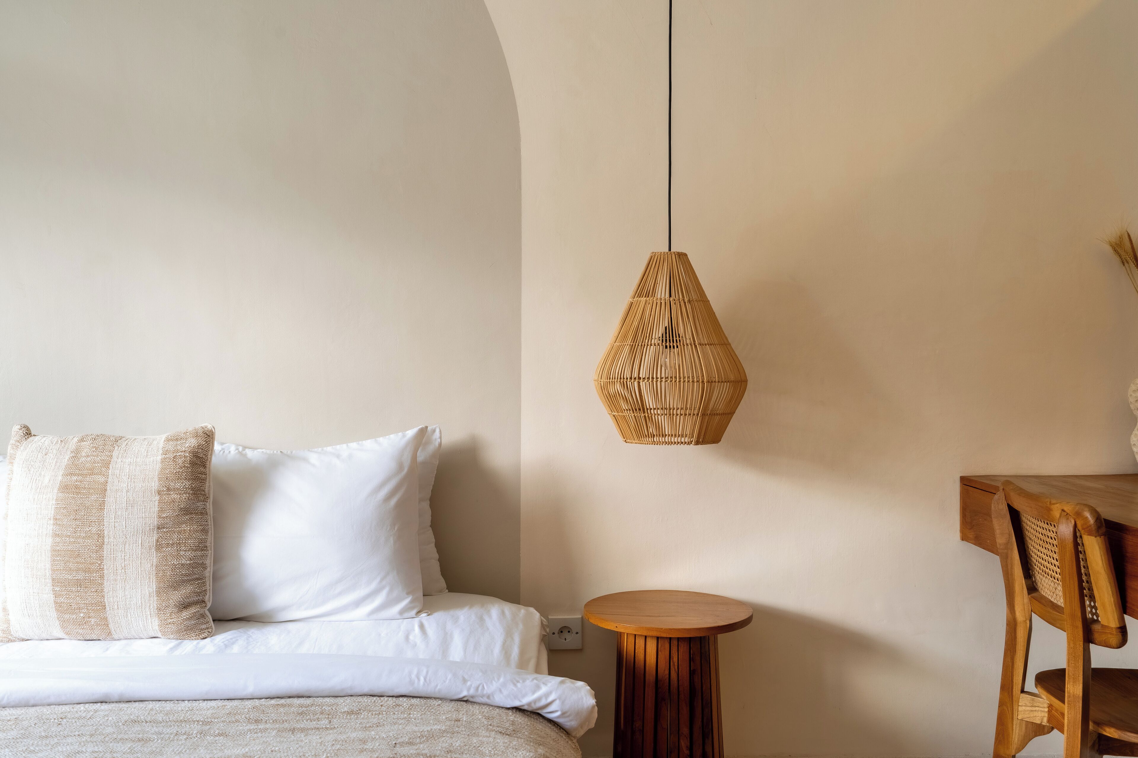 Un dormitorio con una cama, una mesa redonda de madera y una lámpara colgante de fibra.