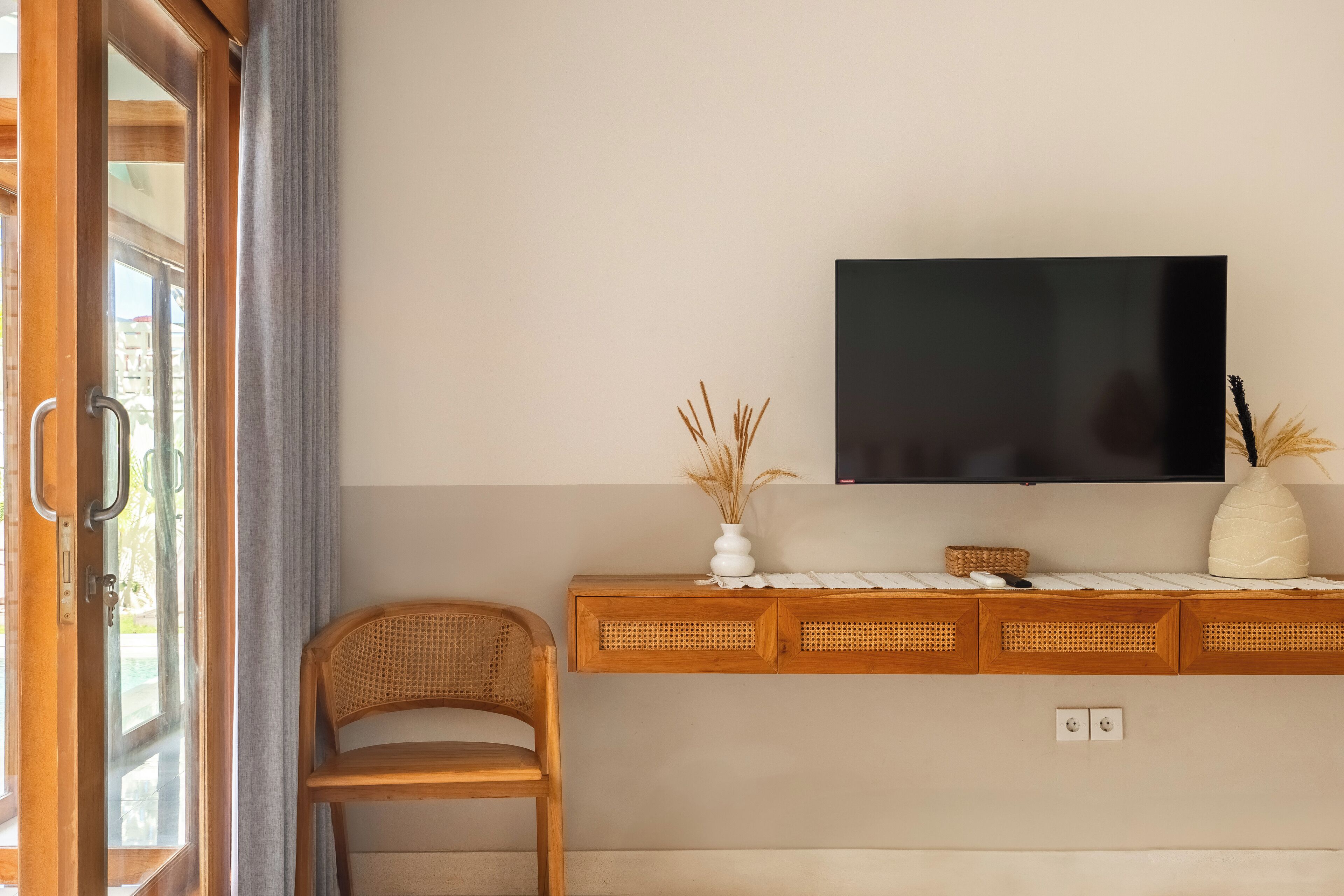 Ein Zimmer mit einem Holzkonsolentisch, einem darüber angebrachten Fernseher und einem Korbstuhl.