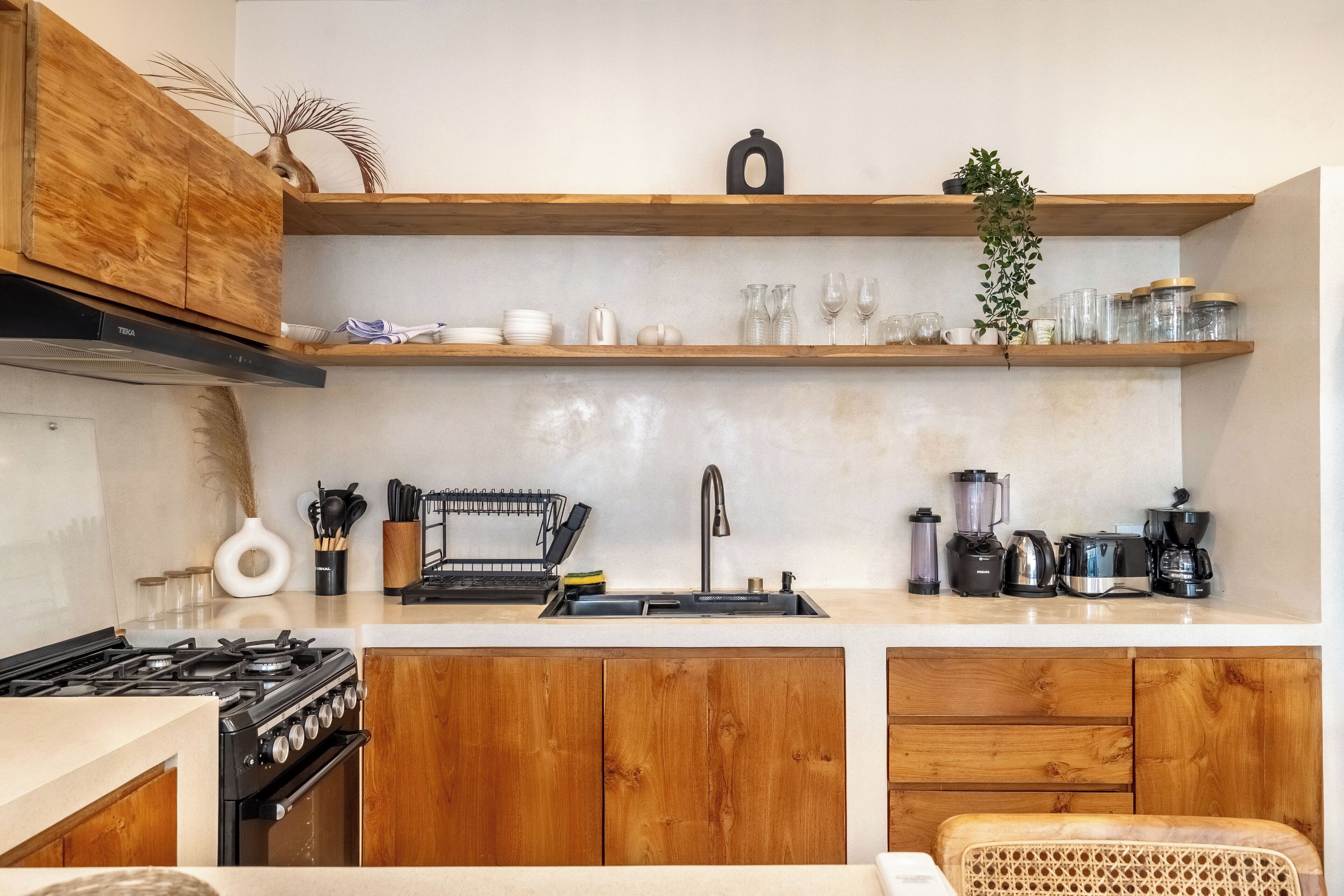 A modern kitchen with wooden cabinets, a stainless steel sink, and various appliances including a stove, blender, and coffee maker.
