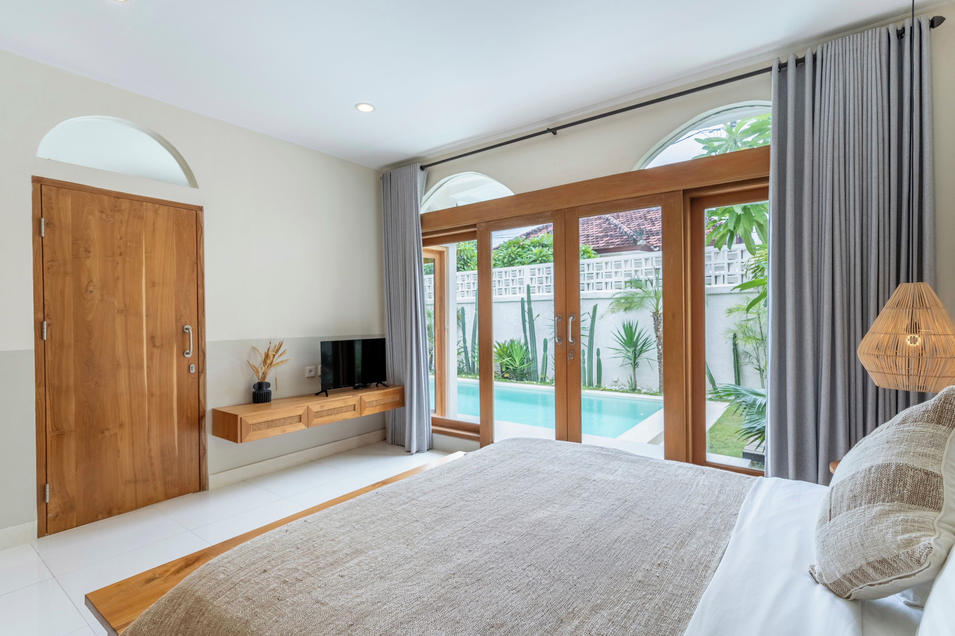 Un dormitorio con una cama grande, un armario de madera, un televisor en un estante y vistas a una piscina y zonas verdes.