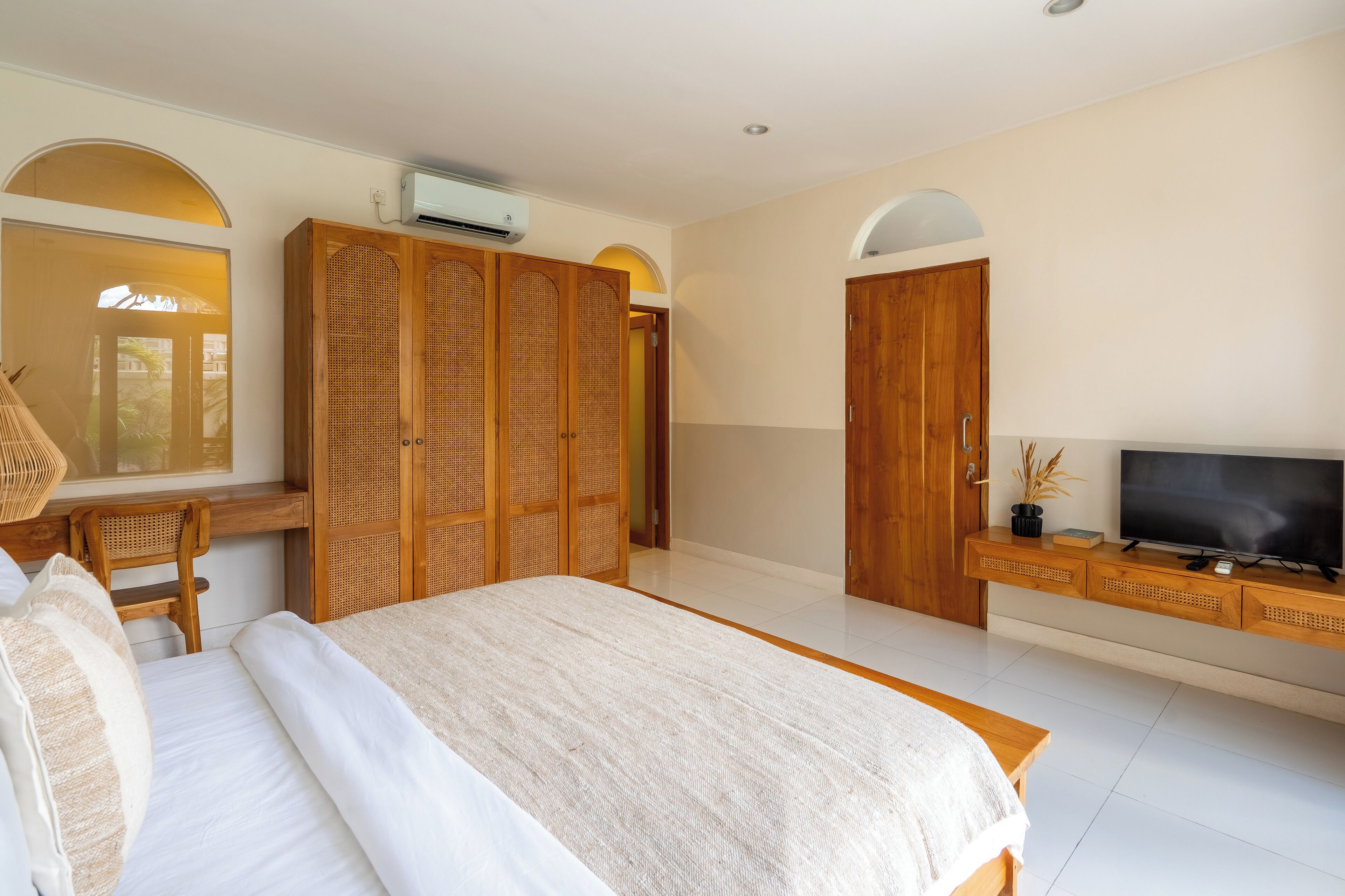Une chambre à coucher avec un grand lit, une armoire en bois, un téléviseur posé sur une console en bois et une fenêtre donnant sur un beau paysage.