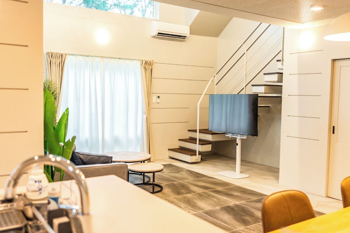 A modern hotel room with a dining area, a staircase, and a large window with curtains.
