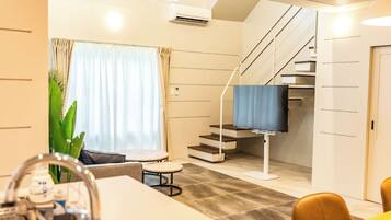 A modern hotel room with a dining area, a staircase, and a large window with curtains.