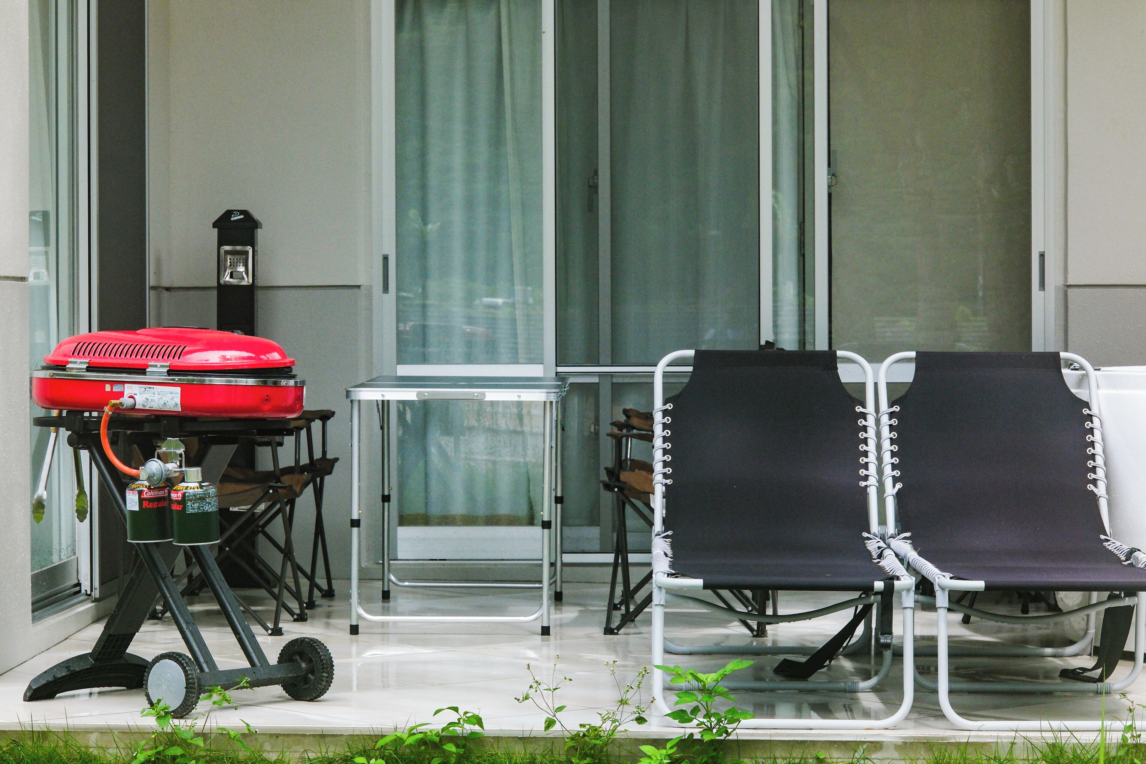 A balcony with a grill, two folding chairs, and a table.