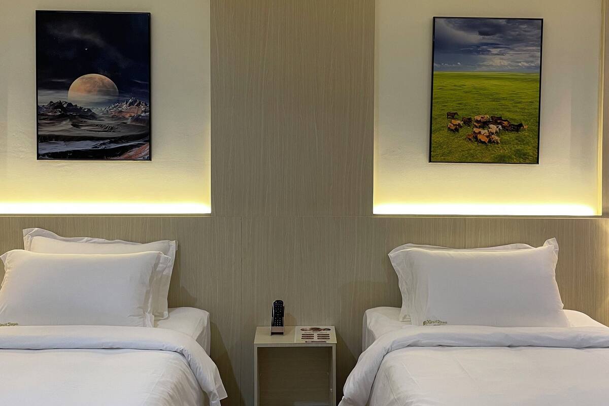 A hotel room with two beds, a nightstand, and two wall-mounted paintings.