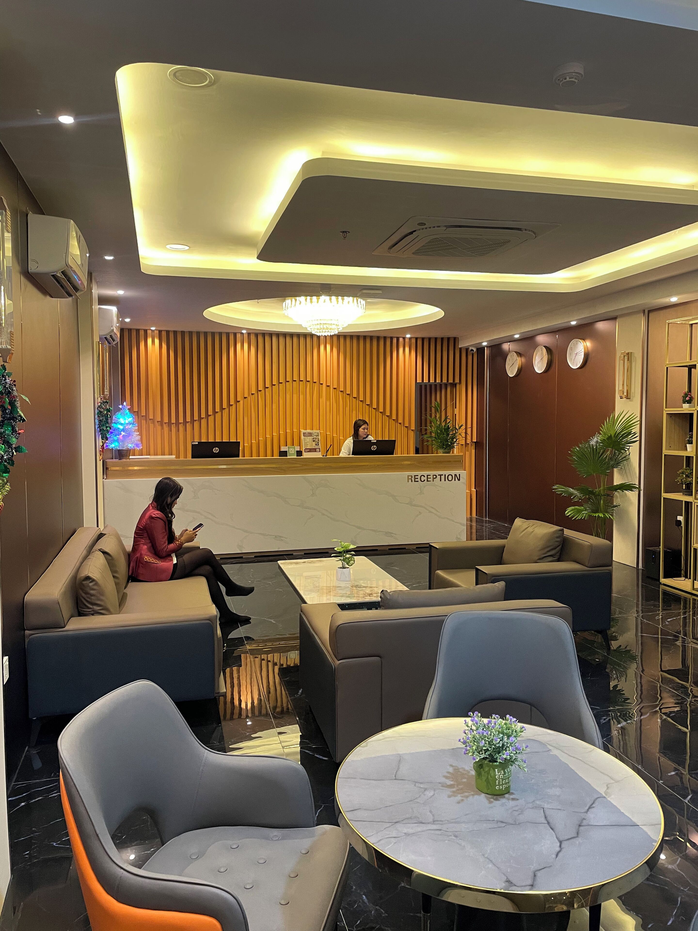 Un'area reception moderna con una receptionist alla scrivania, posti a sedere comodi e un lampadario.