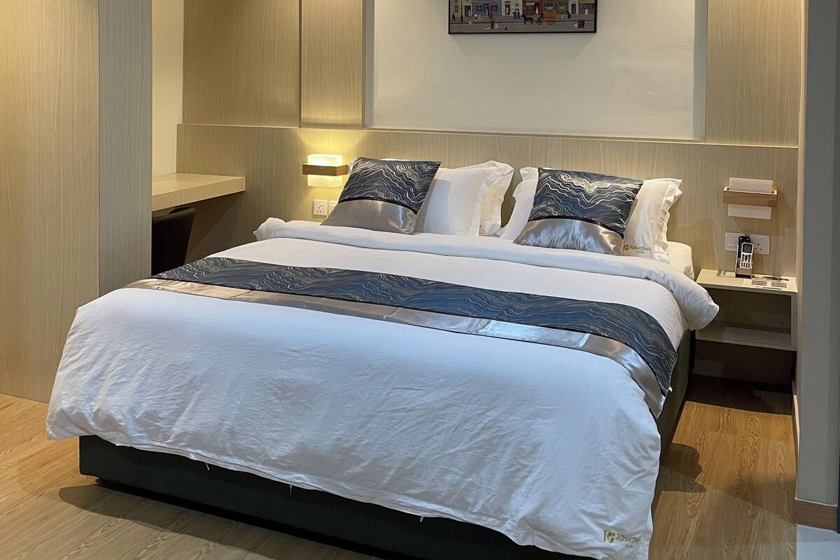 A modern hotel room with a large bed, a painting of a cityscape, and a bedside table with a lamp.