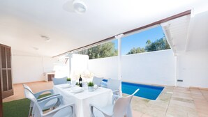 Un'area patio con tavolo da pranzo per quattro persone, una piscina e una zona salotto coperta.
