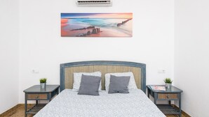 Camera da letto con un letto, due comodini, un condizionatore d'aria a parete e un quadro raffigurante una spiaggia.