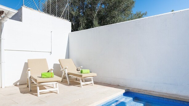 Una piscina con gradini che vi conducono, circondata da pareti bianche e due poltrone beige con cuscini verdi.