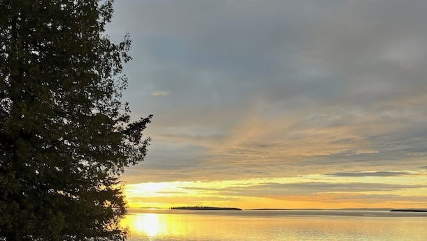 Um terraço com cadeiras Adirondack e uma lareira de pedra com vista para o pôr do sol sobre a água.