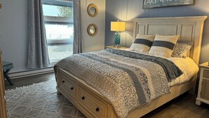 Quarto com cama, mesa de cabeceira, luminária e um aviso na parede.