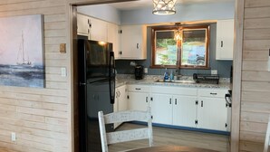 Uma cozinha moderna com armários brancos, uma geladeira preta e uma mesa de jantar de madeira.