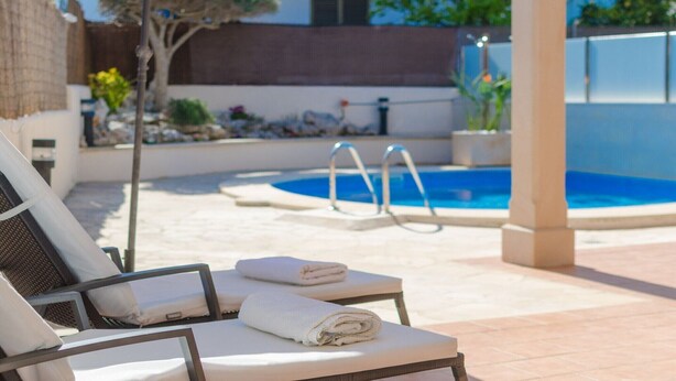 Et poolområde med liggestole, en pool og en pergola.