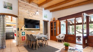 A cozy living area with a wooden interior, a dining table set for four, a television mounted on the wall, and a large wooden cabinet. - Ca Na Rosa - Villa With Private Pool In Campanet (Campanet, Illes Balears)