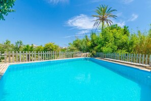 Une piscine rectangulaire entourée d’une clôture en bois, au milieu d’une végétation luxuriante et de palmiers.