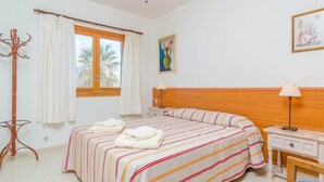 A hotel room with a bed, a nightstand, a lamp, a coat rack, and a window with curtains.