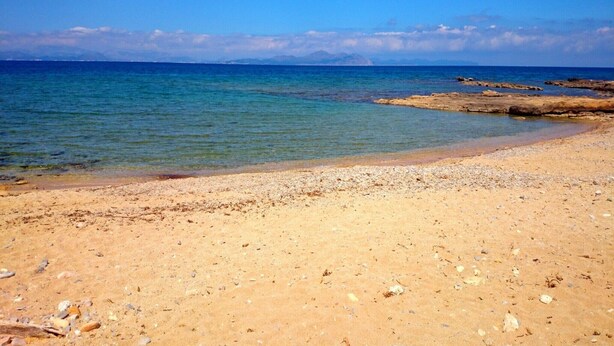 A sandy beach with clear water and rocky outcrops.