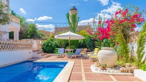 A pool area with a clear blue pool, lounge chairs, and a large decorative pot.
