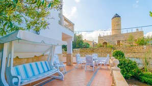 A patio with a swing chair, a table, and chairs, a stone wall, and a tower in the background.