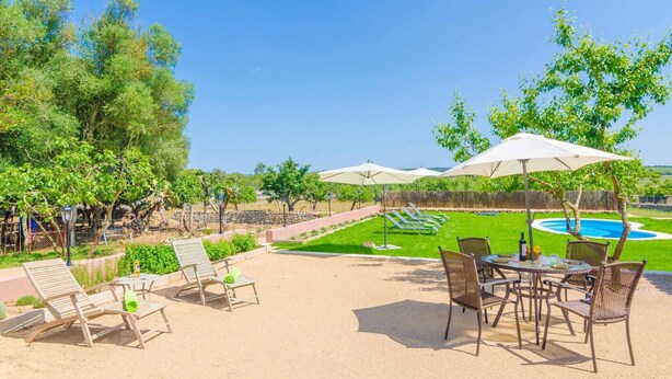 A patio area with lounge chairs, a table, and umbrellas, overlooking a swimming pool and landscaped garden. - Can Potdir - Villa With Private Pool In Ariany (Ariany, Illes Balears)