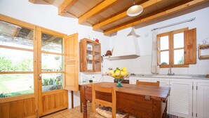 A kitchen with wooden cabinets, a dining table with chairs, and a window with a view of greenery. - Ses Planes (ca Na Faustina) - Villa With Pool (Selva, Illes Balears)