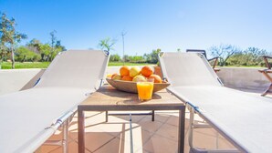 A sunlit outdoor seating area with two lounge chairs and a table holding a bowl of fruit and a glass of orange juice. - Ses Planes (ca Na Faustina) - Villa With Pool (Selva, Illes Balears)